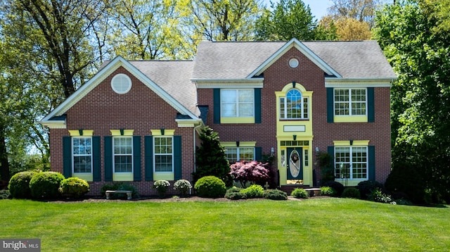 view of front of house with brick siding, a shingled roof, and a front yard