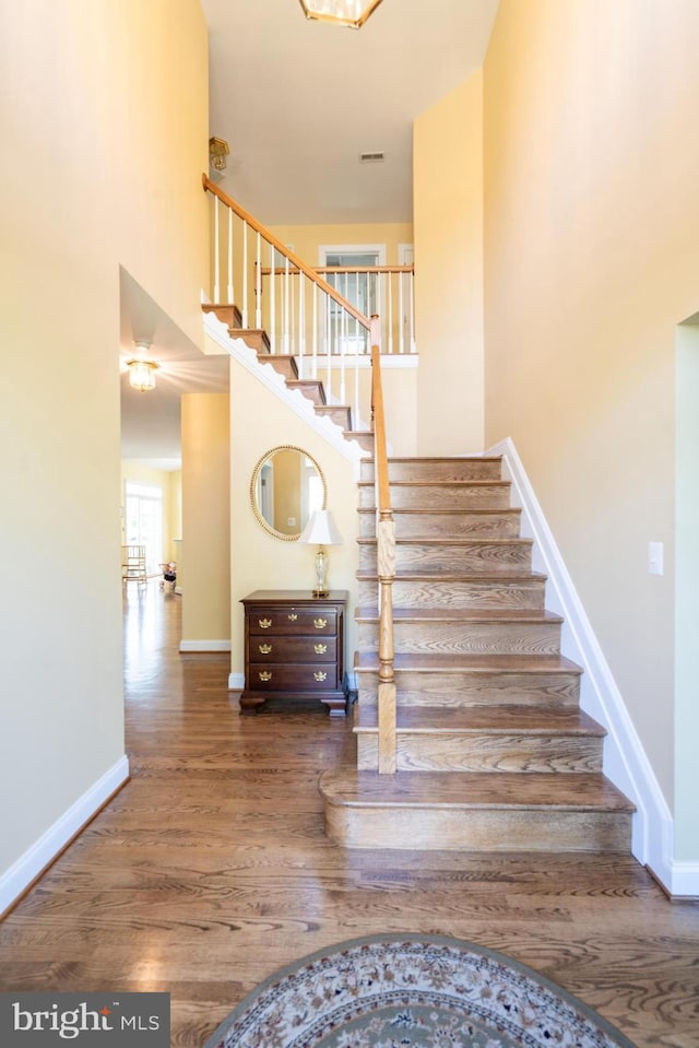 stairway with baseboards, visible vents, wood finished floors, and a high ceiling