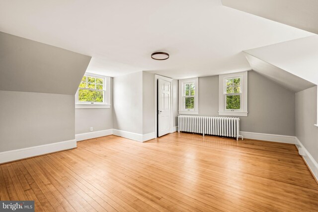 additional living space with light wood-type flooring, baseboards, radiator heating unit, and vaulted ceiling