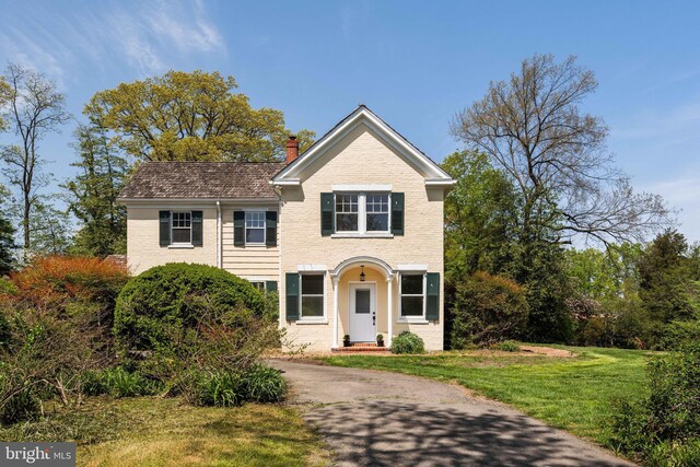 traditional-style home with brick siding, driveway, a front yard, and a chimney