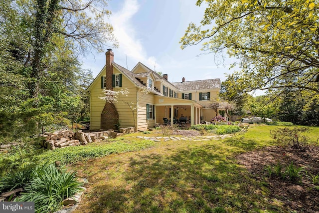 rear view of house with a lawn, a patio, and a chimney