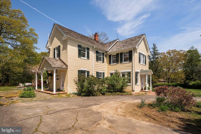 view of side of property with brick siding, a chimney, and a porch