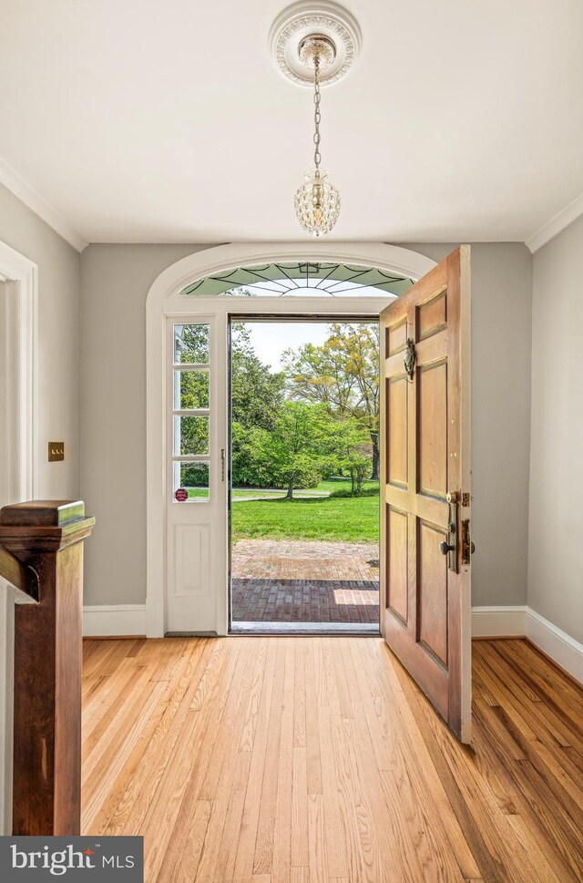 foyer entrance with baseboards, a chandelier, ornamental molding, and light wood finished floors