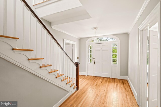 entryway with crown molding, stairs, baseboards, and light wood-style flooring