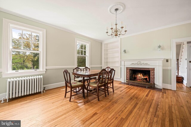 dining space with a notable chandelier, light wood-style floors, built in shelves, radiator, and ornamental molding