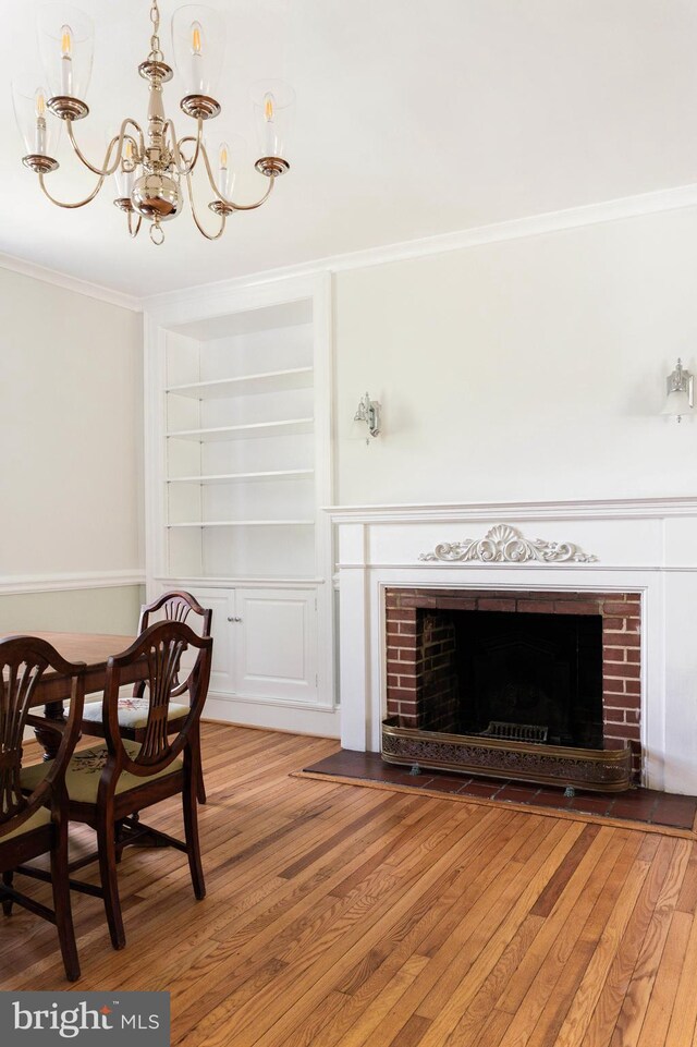 dining space with ornamental molding, a fireplace, built in shelves, light wood-style flooring, and a notable chandelier