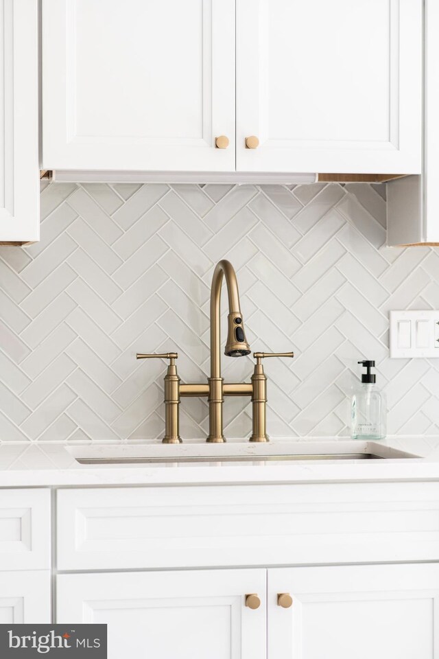 room details featuring a sink, light countertops, white cabinets, and tasteful backsplash