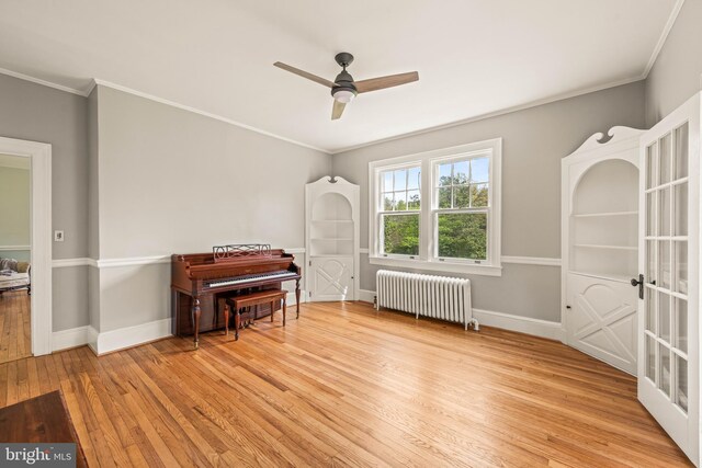 living area featuring light wood-style floors, radiator, a ceiling fan, baseboards, and ornamental molding