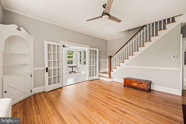 unfurnished living room featuring crown molding, hardwood / wood-style floors, baseboards, stairway, and a ceiling fan