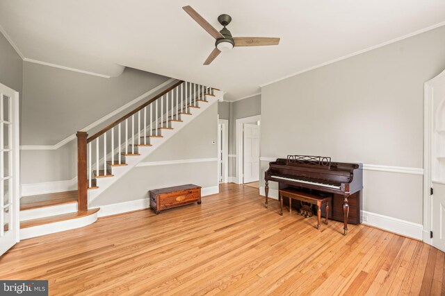 living area with wood-type flooring, ornamental molding, baseboards, ceiling fan, and stairway