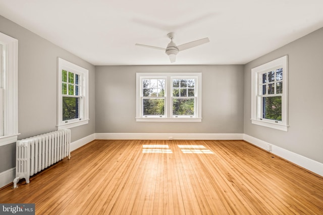 empty room featuring light wood-style floors, radiator, baseboards, and a ceiling fan