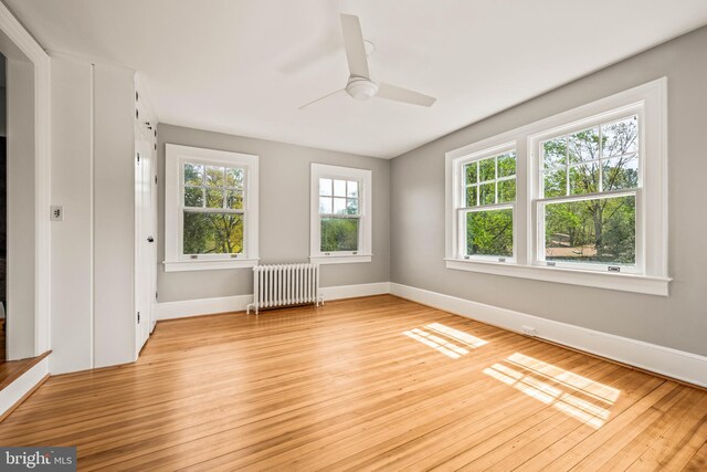 unfurnished room with baseboards, light wood finished floors, radiator heating unit, and a healthy amount of sunlight
