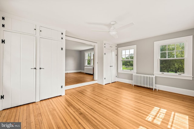 unfurnished bedroom with baseboards, multiple closets, radiator, and light wood-type flooring