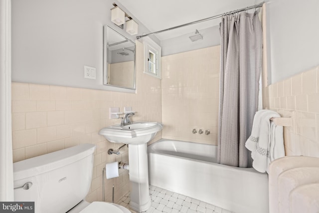 full bath with tile patterned flooring, shower / tub combo with curtain, wainscoting, toilet, and tile walls