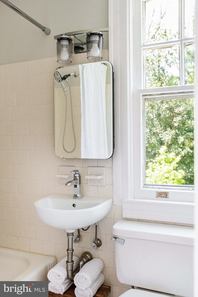 full bath featuring a sink, shower / bath combo, toilet, tile walls, and backsplash