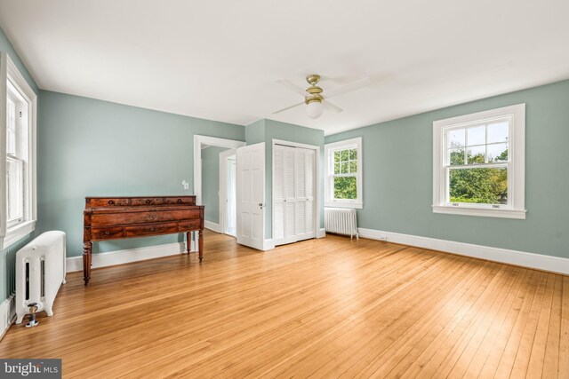 bedroom with light wood-style floors, baseboards, ceiling fan, and radiator heating unit