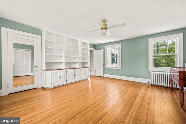 interior space with radiator heating unit, baseboards, a ceiling fan, and light wood finished floors