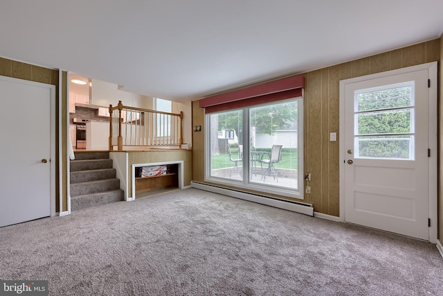 unfurnished living room with wood walls, baseboard heating, carpet flooring, and stairs