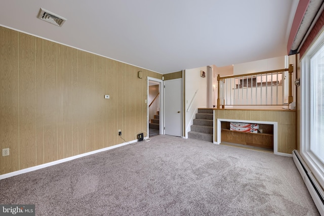 unfurnished living room with visible vents, baseboard heating, stairway, wooden walls, and carpet flooring