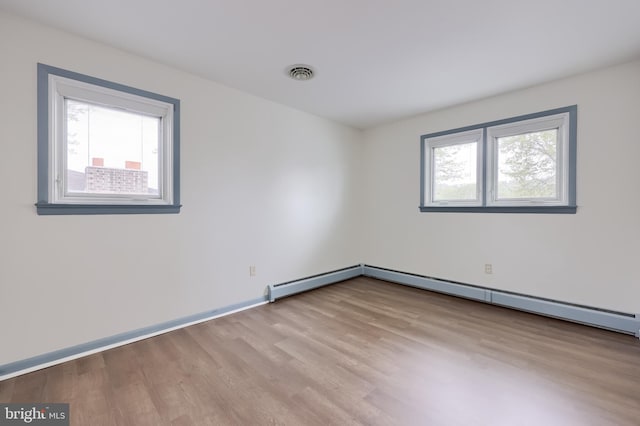 empty room with baseboard heating, baseboards, visible vents, and wood finished floors