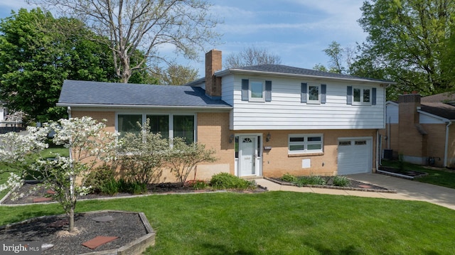 split level home featuring a front lawn, a chimney, brick siding, concrete driveway, and an attached garage