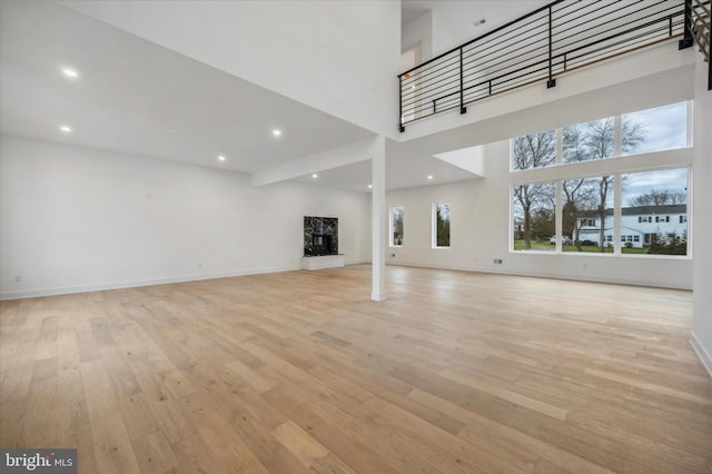 unfurnished living room featuring recessed lighting, baseboards, a high ceiling, and light wood finished floors