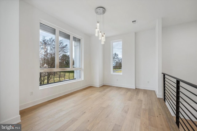 spare room with baseboards, a notable chandelier, light wood-style flooring, and visible vents