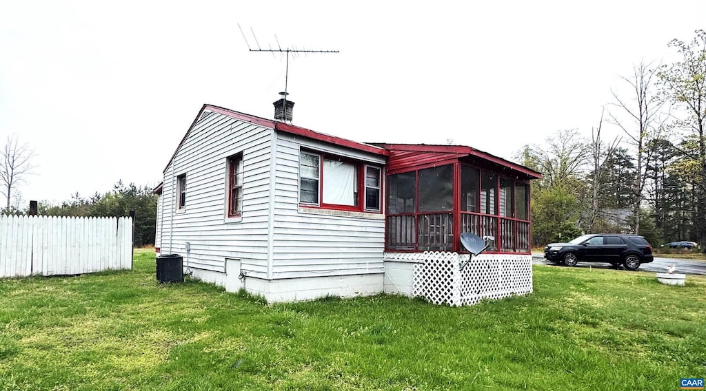 view of side of home with fence, cooling unit, a chimney, a sunroom, and a lawn