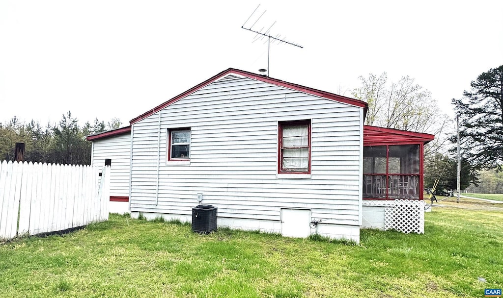 view of side of property featuring central air condition unit, a lawn, fence, and a sunroom