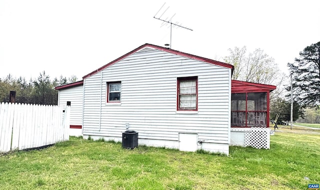 view of side of property featuring central air condition unit, a lawn, fence, and a sunroom