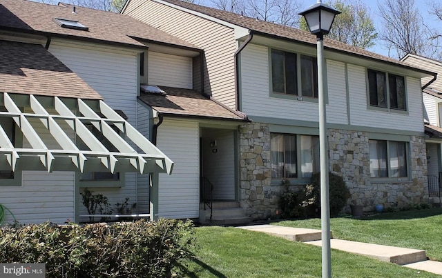 view of front facade with a shingled roof, a front lawn, and stone siding