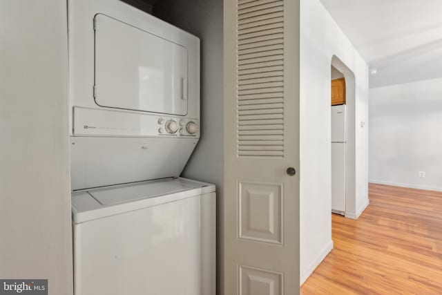 laundry area with baseboards, stacked washer / drying machine, light wood-type flooring, and laundry area