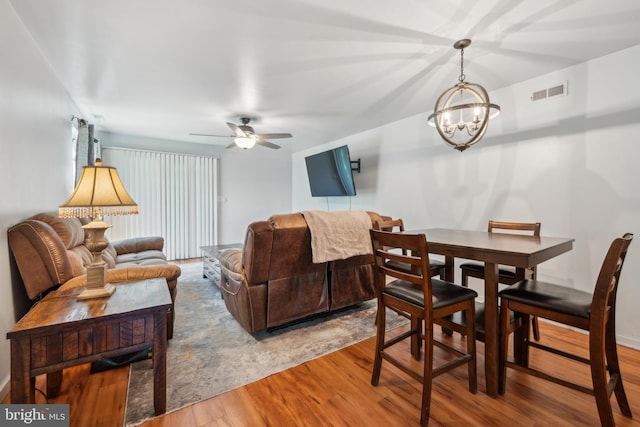 living area with visible vents, wood finished floors, and ceiling fan with notable chandelier