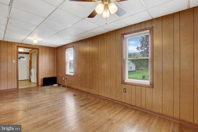 unfurnished room with a ceiling fan, a drop ceiling, wood walls, and hardwood / wood-style flooring