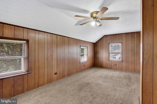 carpeted spare room with a ceiling fan, wood walls, and lofted ceiling