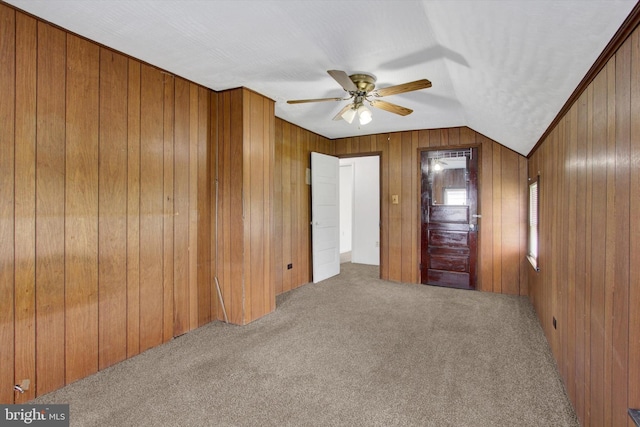 unfurnished bedroom with carpet flooring, ceiling fan, wood walls, and lofted ceiling