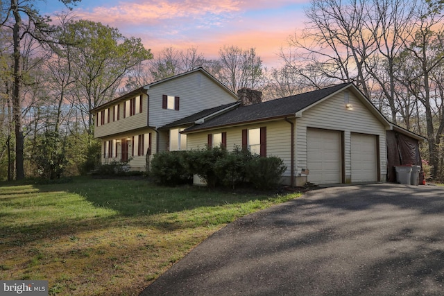 view of front of house with a chimney, an attached garage, driveway, and a front yard