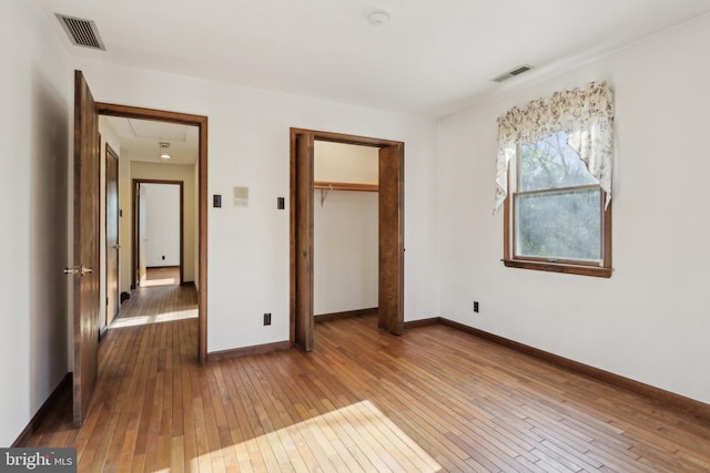 unfurnished bedroom featuring visible vents, attic access, wood-type flooring, and baseboards