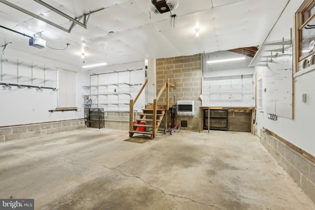 garage featuring a garage door opener, heating unit, and concrete block wall