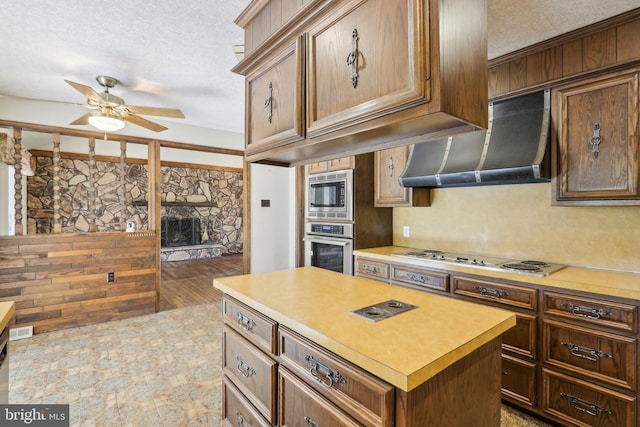 kitchen with stainless steel appliances, a textured ceiling, ceiling fan, and wall chimney exhaust hood
