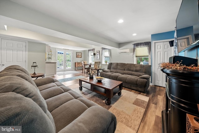 living area with wood finished floors, recessed lighting, a wall unit AC, and french doors