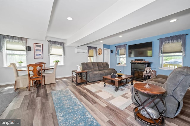 living room featuring baseboards, a wall mounted air conditioner, a glass covered fireplace, and wood finished floors