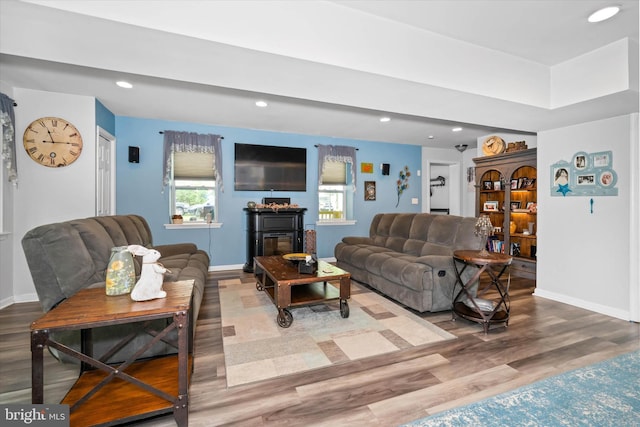 living area featuring a glass covered fireplace, baseboards, recessed lighting, and wood finished floors