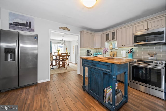 kitchen with stainless steel appliances, cream cabinetry, dark wood-type flooring, backsplash, and butcher block counters