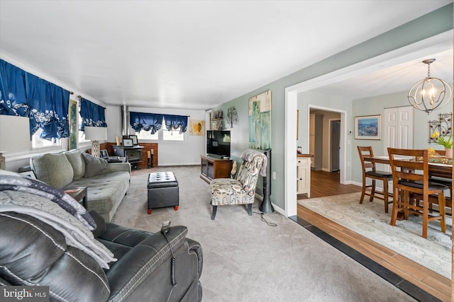 carpeted living room with baseboards, a notable chandelier, wood finished floors, and a wood stove