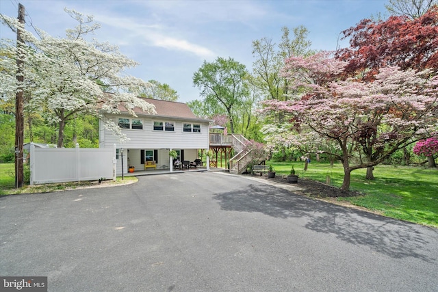 view of front of property featuring aphalt driveway, a wooden deck, fence, a front yard, and stairs