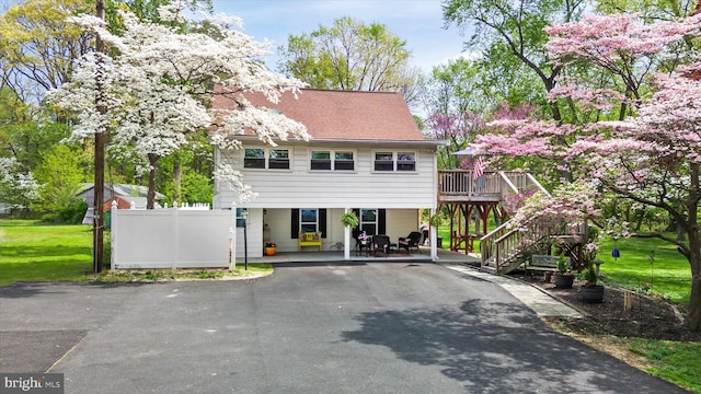 view of front of house with driveway, a deck, fence, a front lawn, and stairs