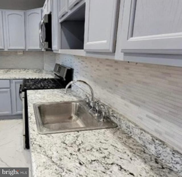 kitchen featuring a sink, appliances with stainless steel finishes, decorative backsplash, and light stone counters