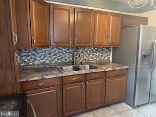 kitchen with decorative backsplash, range, a sink, stainless steel fridge, and light tile patterned flooring