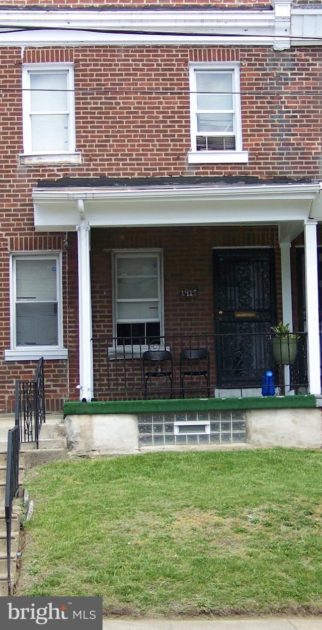 entrance to property with covered porch, brick siding, and a yard
